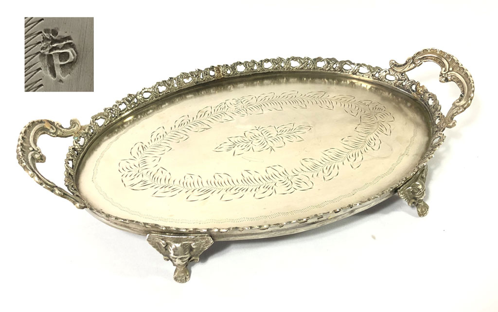 PRATA P COROA. Elegante bandeja em formato oval, tendo galeria rendilhada a volta, pegas e pés ornados com garras e cara de leão em metal espessurado a prata. Sua base oval é feita em Prata P Coroa trabalhada com floráceas. Medidas: 36cm de pega a pega.